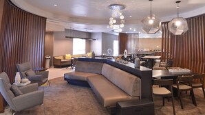 Un moderno vestíbulo de hotel con un sofá curvo, zona de comedor y cocina al fondo.