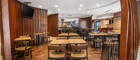 A restaurant with wooden panel walls, multiple seating areas, and a central kitchen visible through an open space.