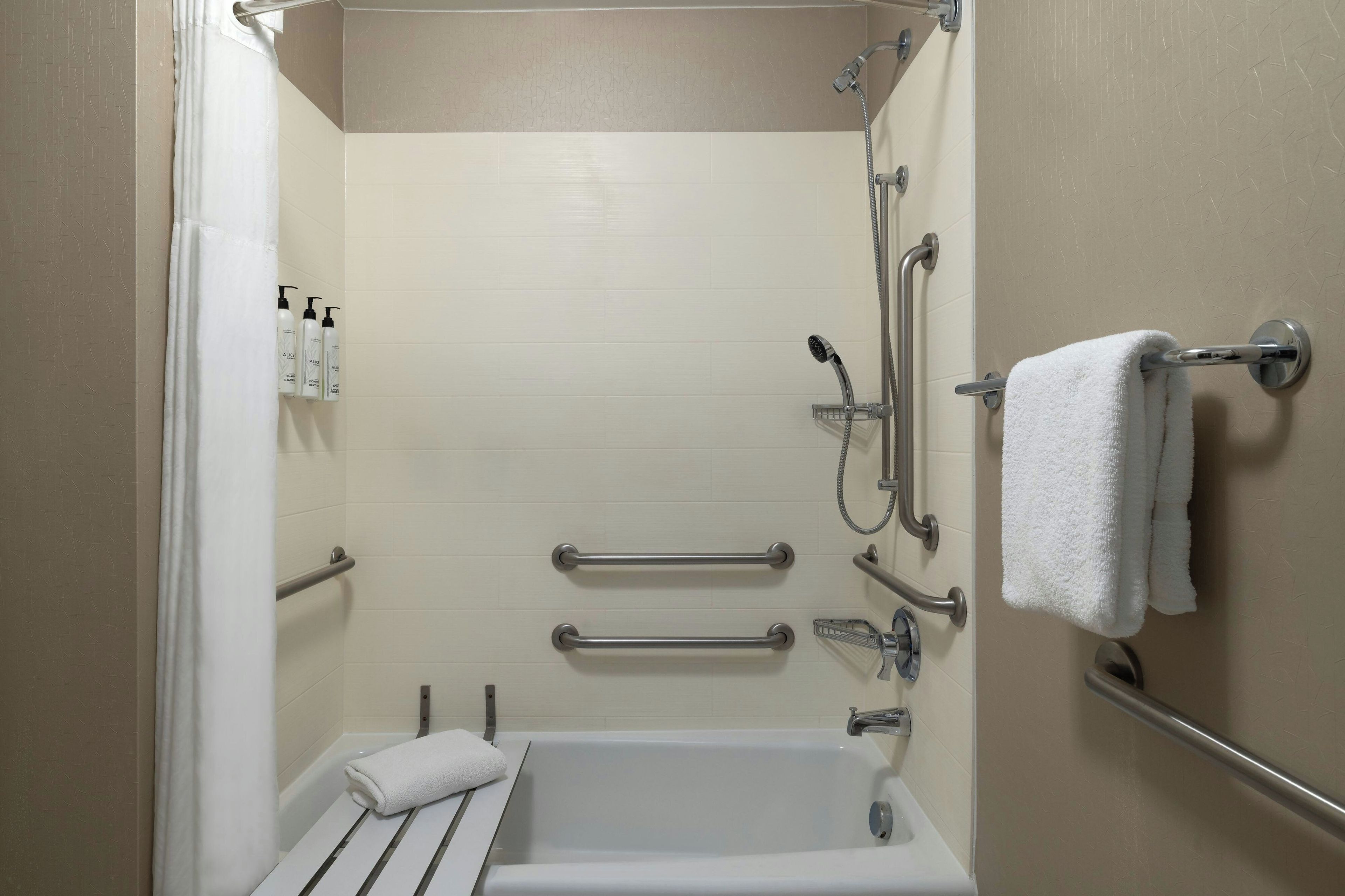 A bathroom with a bathtub, a shower, and handrails.