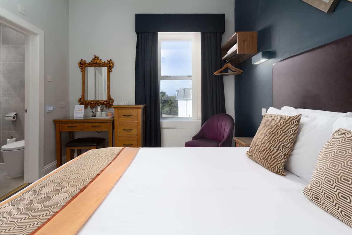 A hotel room with a bed, a desk, a chair, a mirror, and a window with curtains.