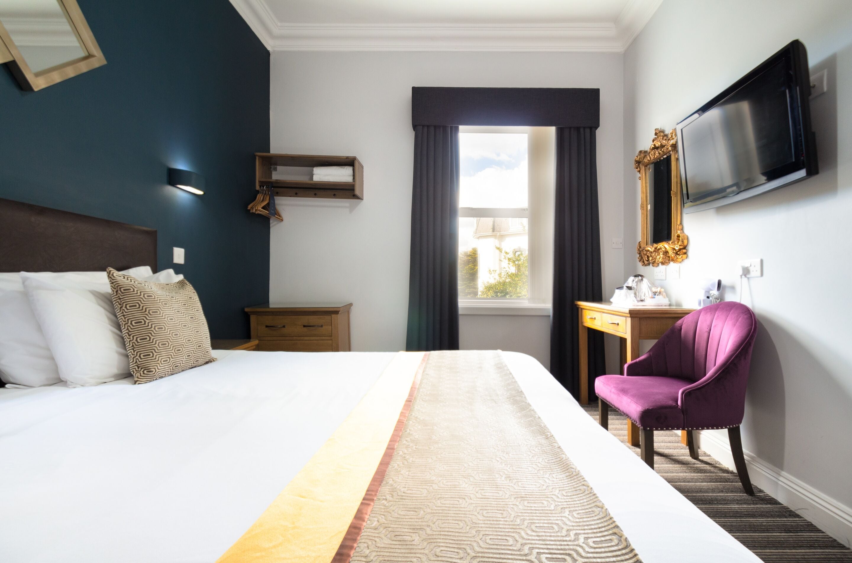 Una habitación de hotel con una cama grande, un escritorio, una silla, un televisor y una ventana con cortinas.