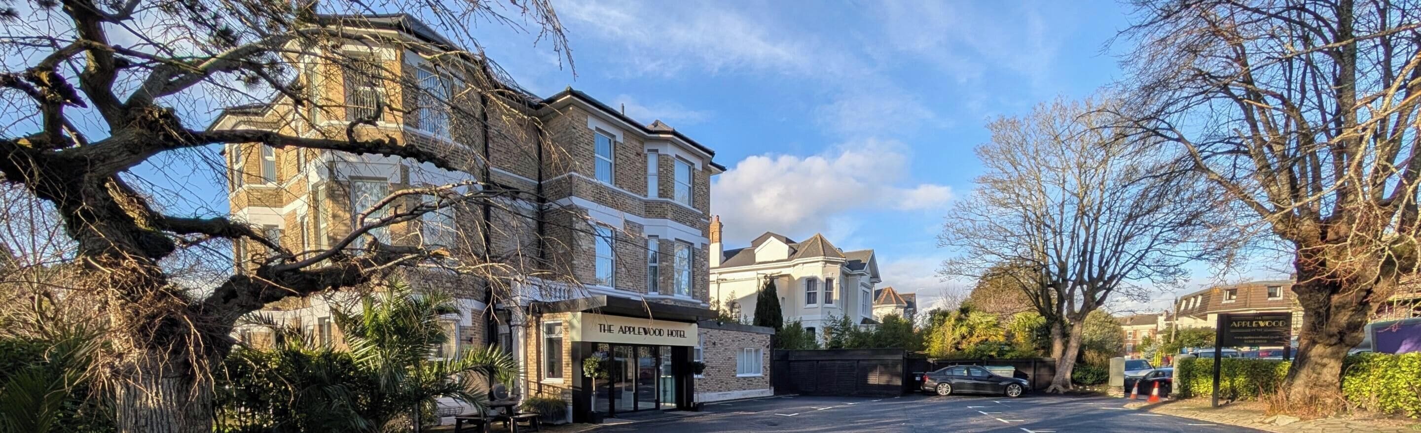 A street view with a hotel named 'The Applewood Hotel' on the left, a large tree in the foreground, and a parked car on the right.