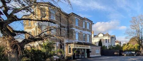 A street view with a hotel named 'The Applewood Hotel' on the left, a large tree in the foreground, and a parked car on the right.