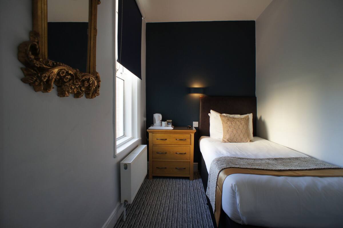A hotel room with a bed, a nightstand with a lamp, a dresser, and a mirror.