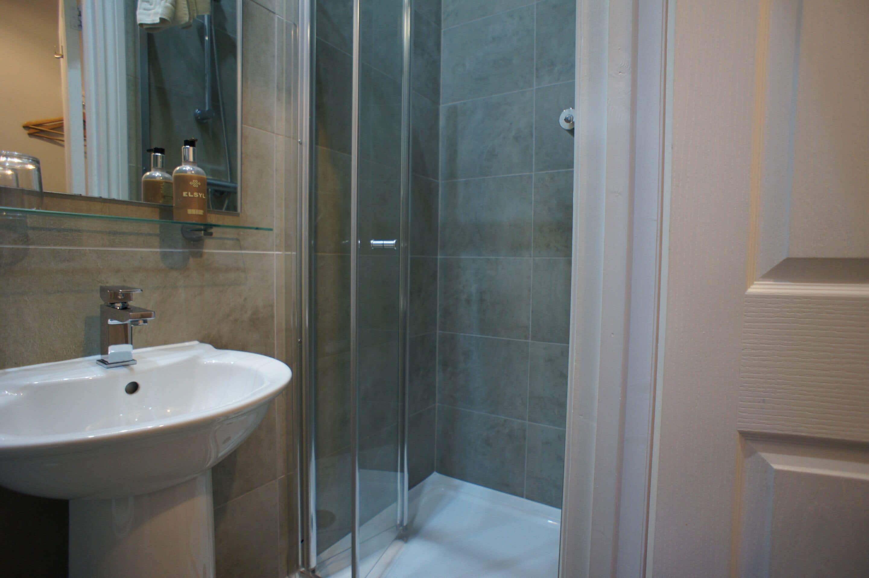 A bathroom with a glass shower enclosure, a white sink, and a mirror above the sink.