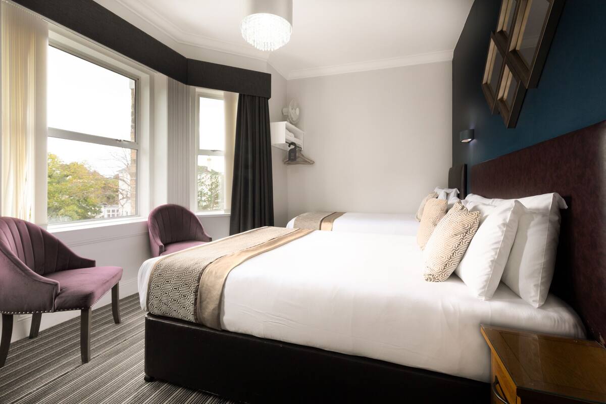 A hotel room with a large bed, a chair, a nightstand, and a window with curtains.