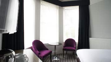 A hotel room with a bed, two purple armchairs, a small round table, and a coffee maker.