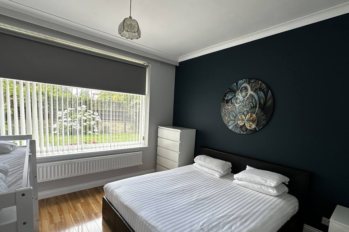 A bedroom with a large bed, a dresser, a radiator, and a window with a view of greenery.
