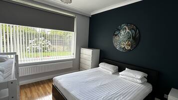 A bedroom with a large bed, a dresser, a radiator, and a window with a view of greenery.