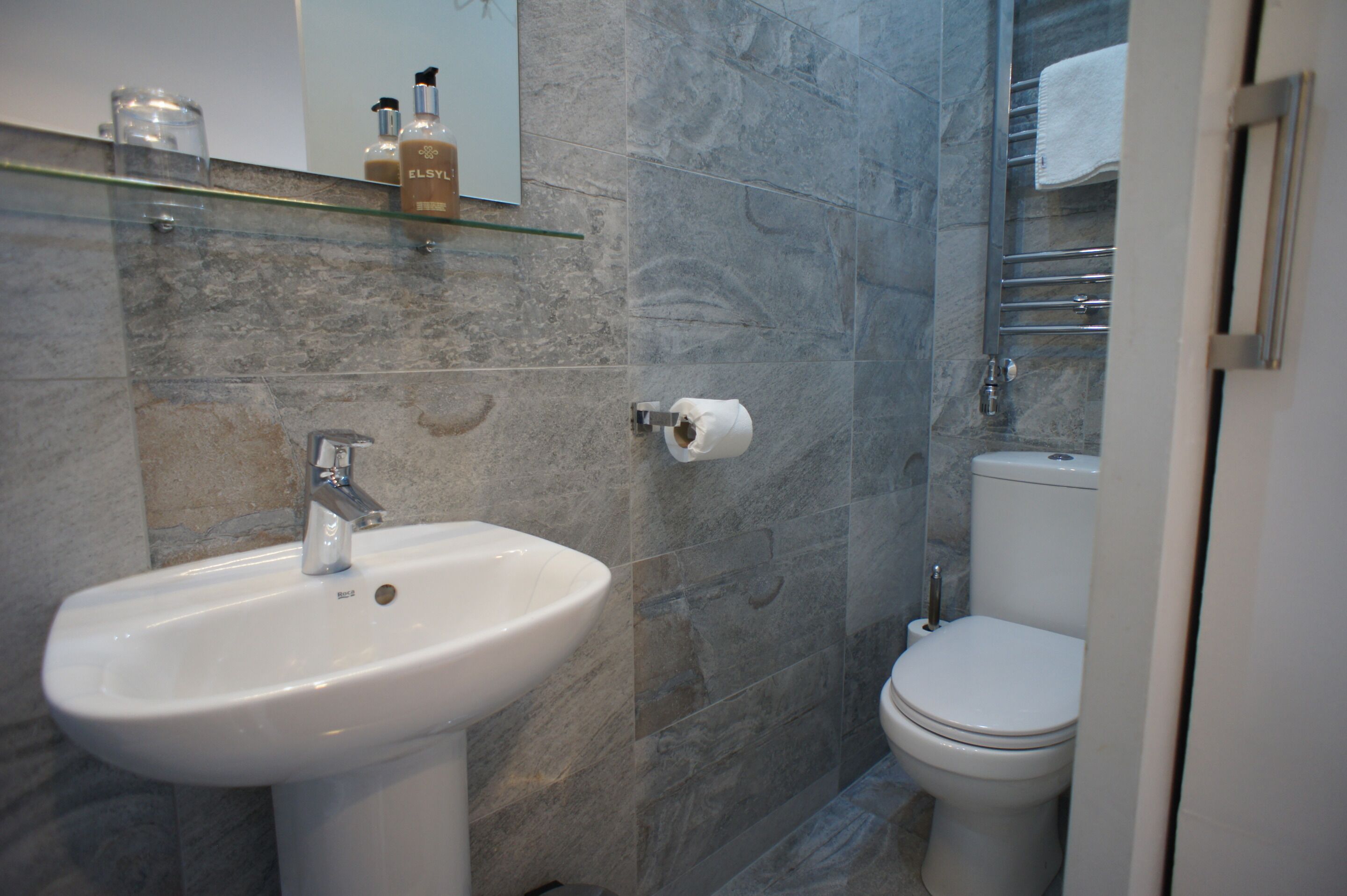 Une salle de bain avec un lavabo blanc, des toilettes et des murs en marbre.