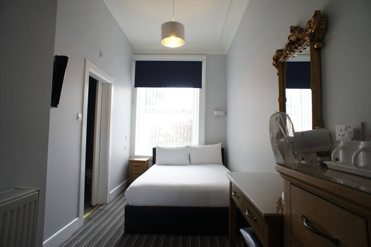 A hotel room with a bed, bedside table, dresser, mirror, and a window with a view.