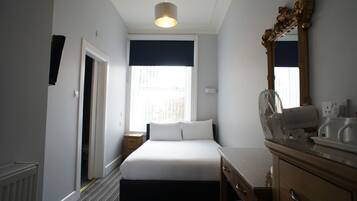 Habitación de hotel con cama, mesita de noche, cómoda, espejo y ventana con vistas.