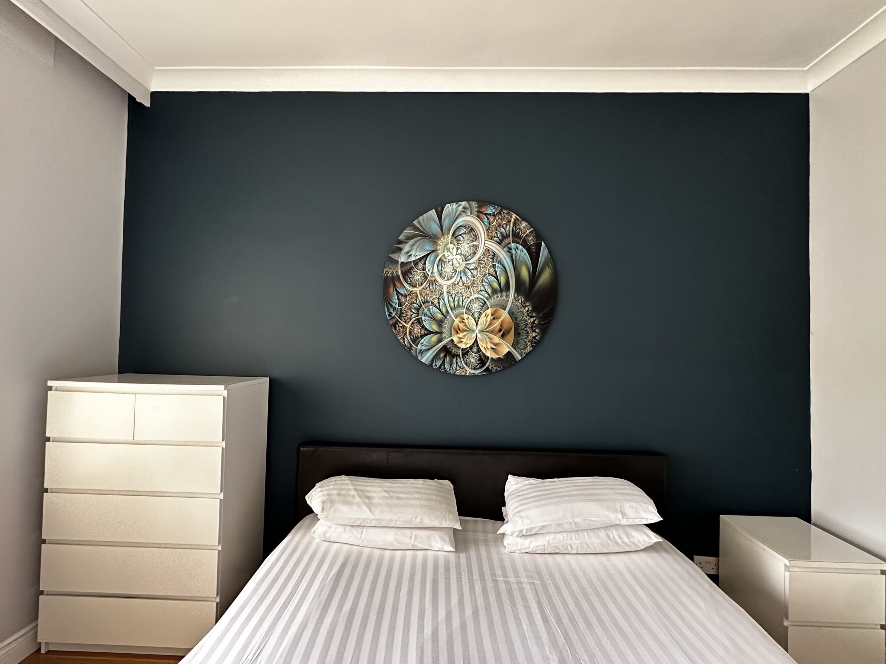 Une chambre à coucher comprenant un lit, deux tables de chevet, une commode et un élément décoratif mural.