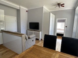 Een moderne woonkamer met een houten eettafel, een televisie op een witte standaard en een plafondventilator.