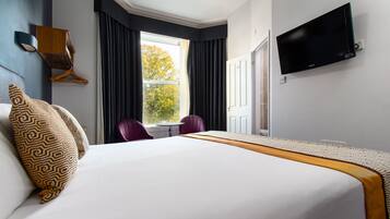Een hotelkamer met een groot bed, een aan de muur bevestigde televisie, een raam met gordijnen en een stoel.