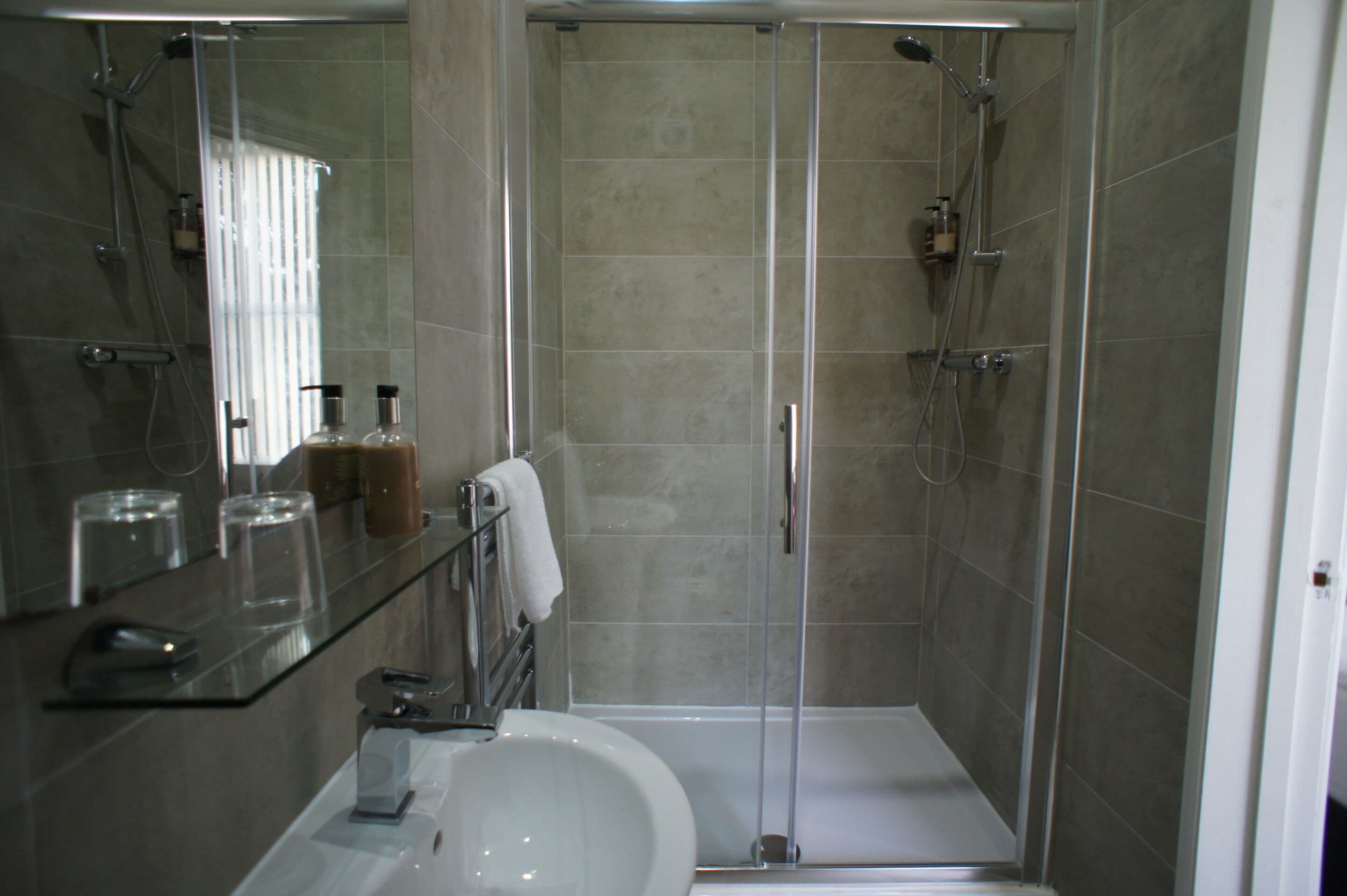 Un baño moderno con ducha envuelta en vidrio, un lavabo con espejo y un estante de vidrio con artículos de aseo.