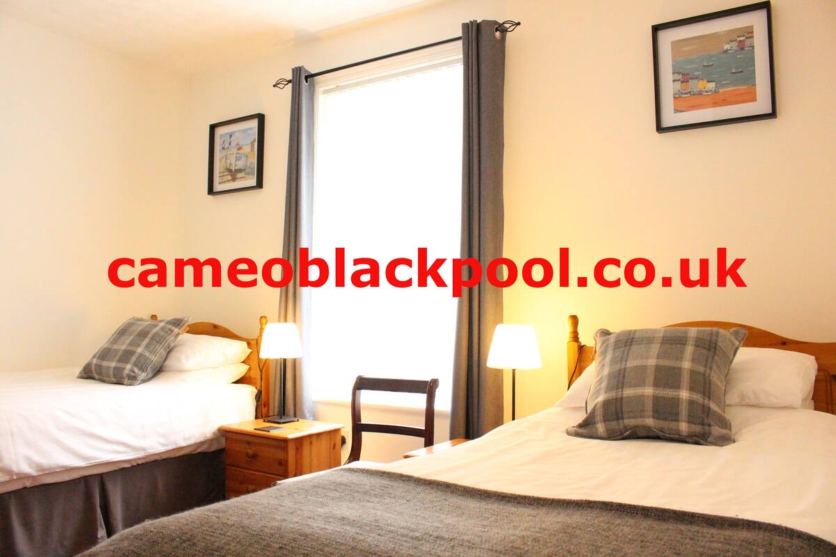 A hotel room with two beds, a chair, a nightstand, and a window with curtains.