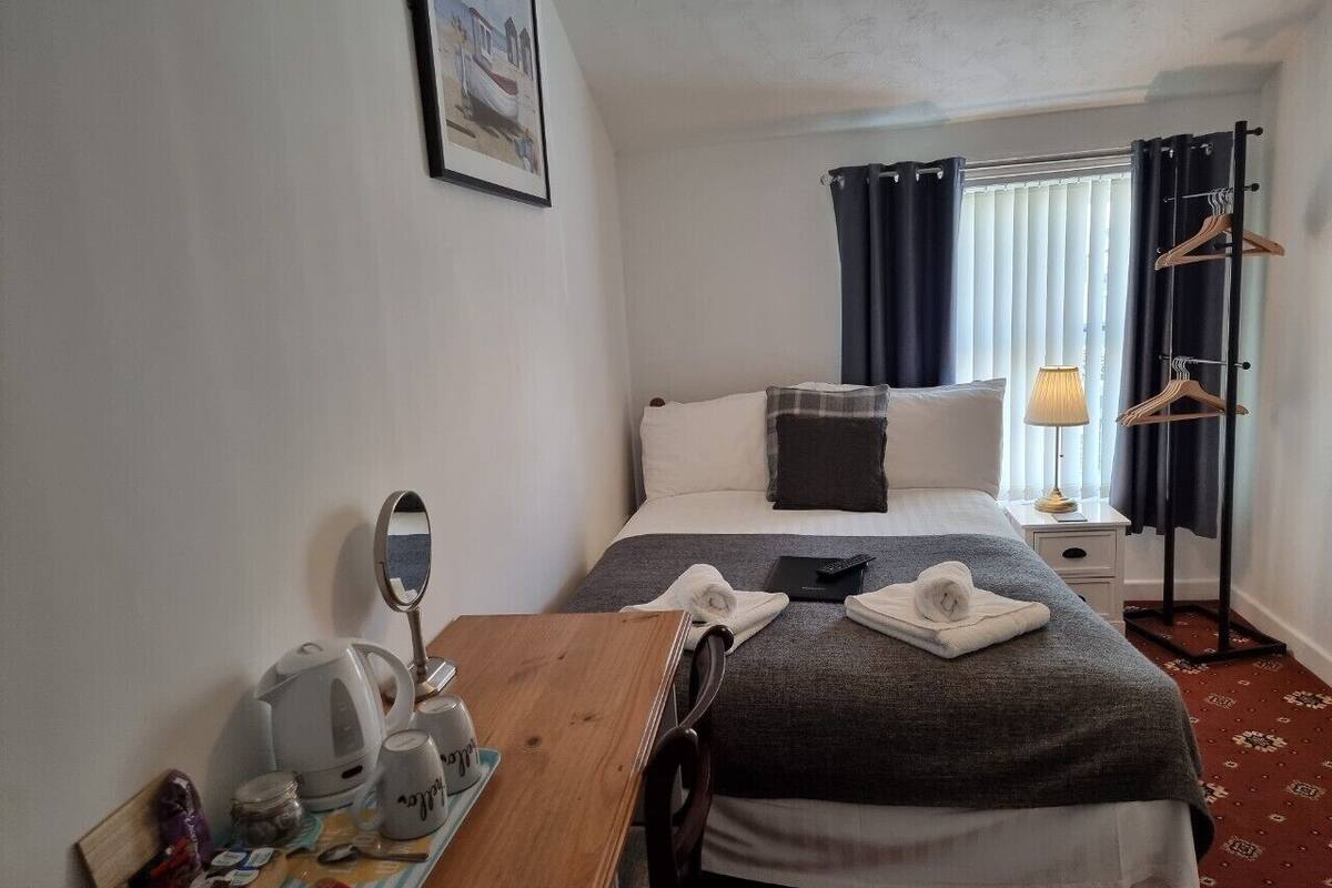 A hotel room with a bed, bedside table, lamp, and a coat rack.