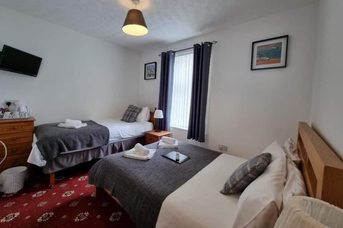 A hotel room with two beds, a TV, a desk with a lamp, and a window with curtains.