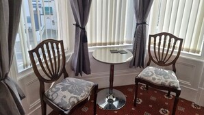 A corner room with two wooden chairs and a small round table, a window with blinds, and a patterned carpet. - The Cameo (Blackpool)