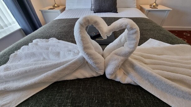 A hotel room with a bed, two bedside tables, lamps, and a heart-shaped towel arrangement on the bed. - The Cameo (Blackpool)