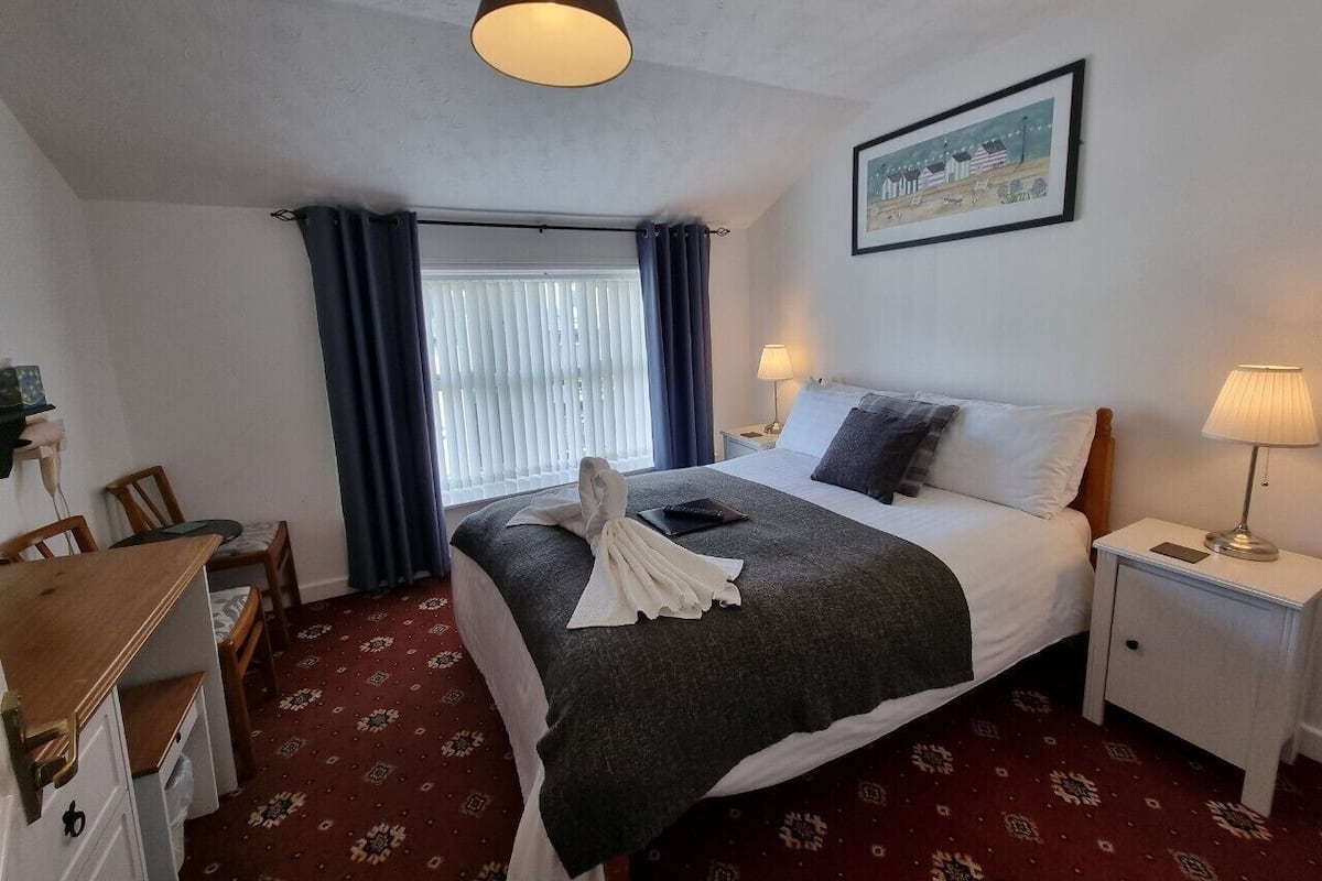 A hotel room with a bed, bedside tables, a desk, and a window with curtains.