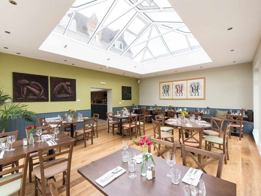 A restaurant with a high ceiling and skylight, wooden tables and chairs, and artwork on the walls.