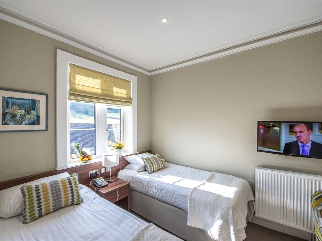 Ett hotellrum med två sängar, ett fönster med persienner, en tv på väggen och ett element.
