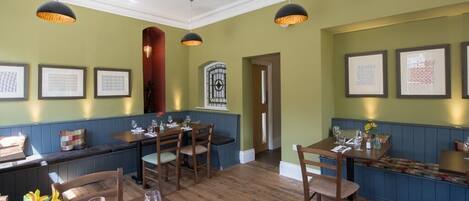 A restaurant with wooden tables and chairs, green walls, and framed artwork.