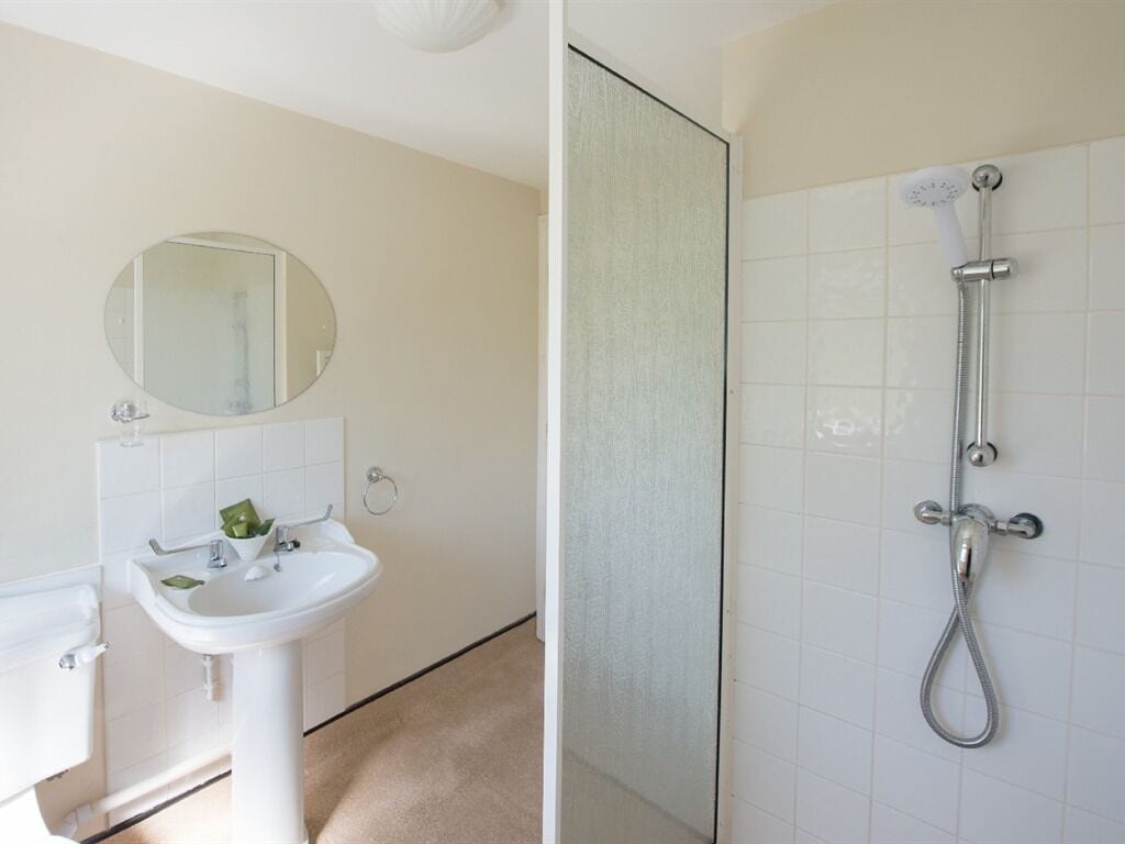 Un baño con lavamanos, espejo y ducha blancos.