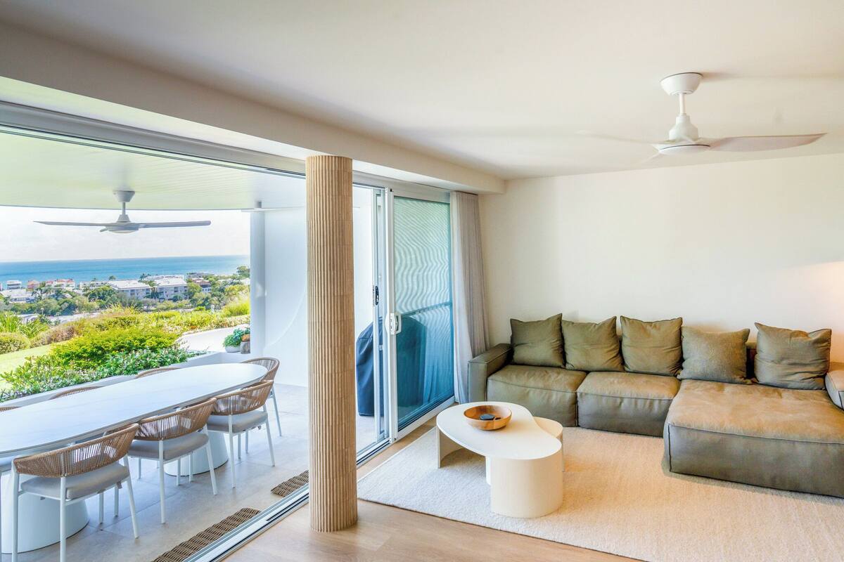 A modern living room with a sofa, a dining table with chairs, a small coffee table, and a view of the outdoors.