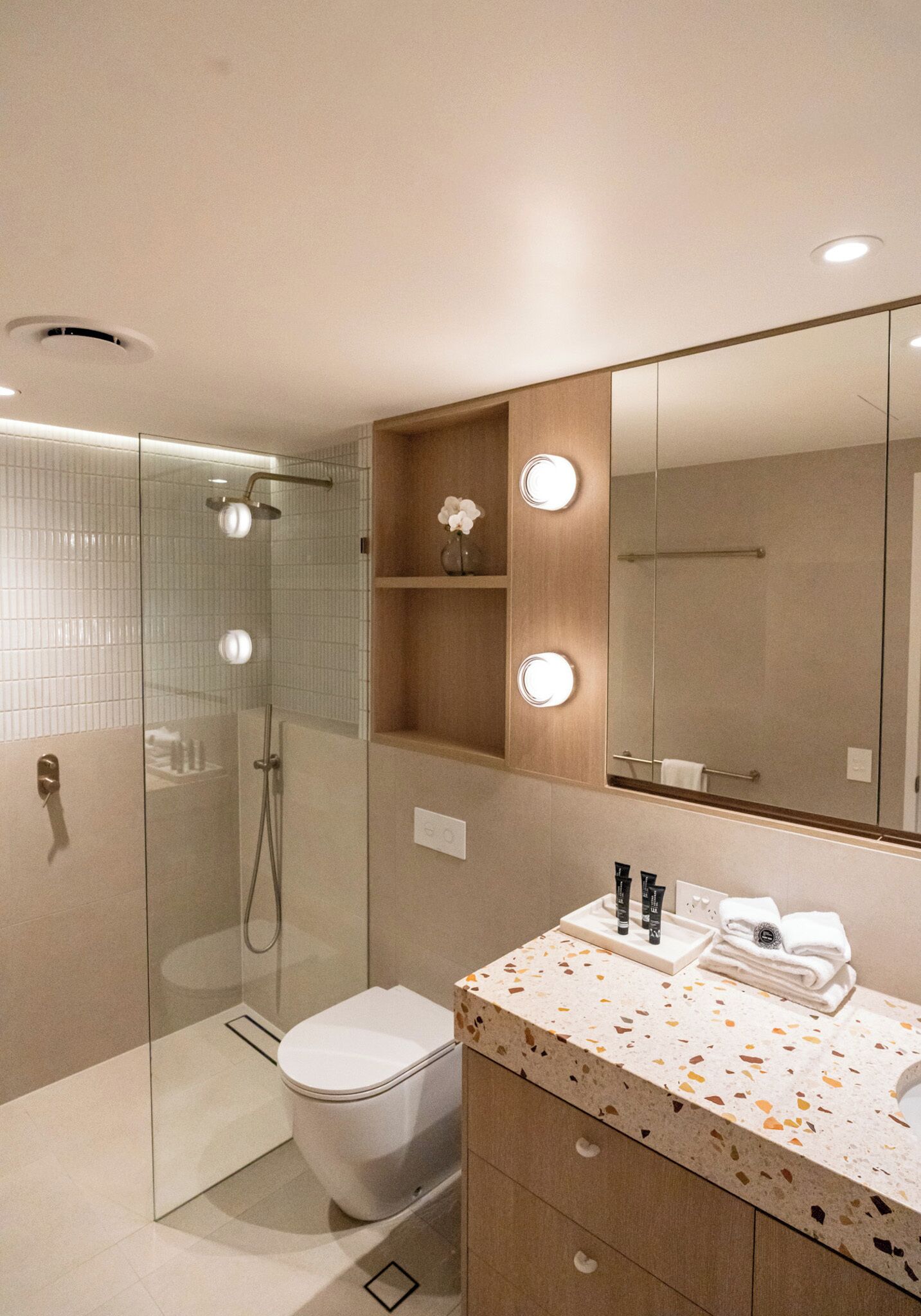 Un baño moderno con ducha de vidrio, inodoro, lavamanos con espejo y tocador con espejo iluminado.