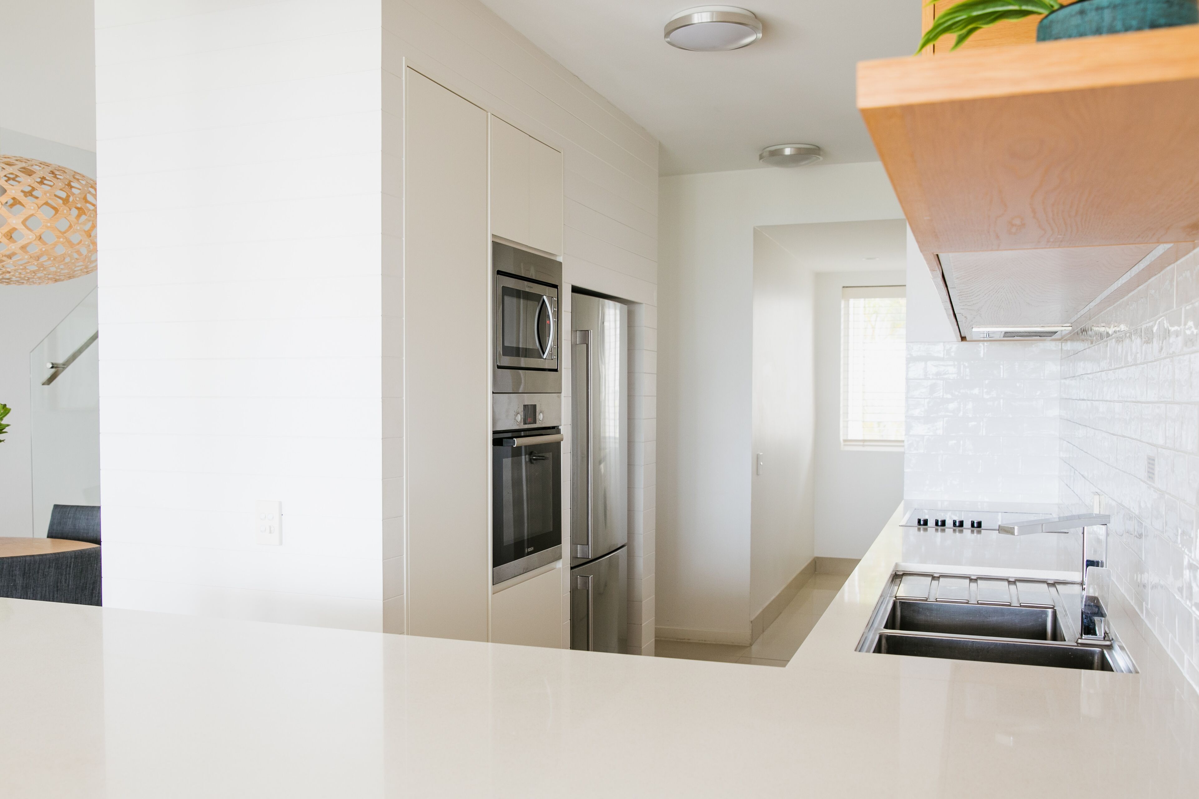 A modern kitchen with stainless steel appliances, a white countertop, and a wooden shelf above the sink.
