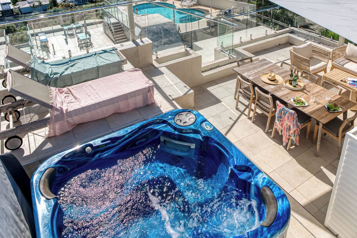 A rooftop pool area with a hot tub, lounge chairs, and a dining table with umbrellas.