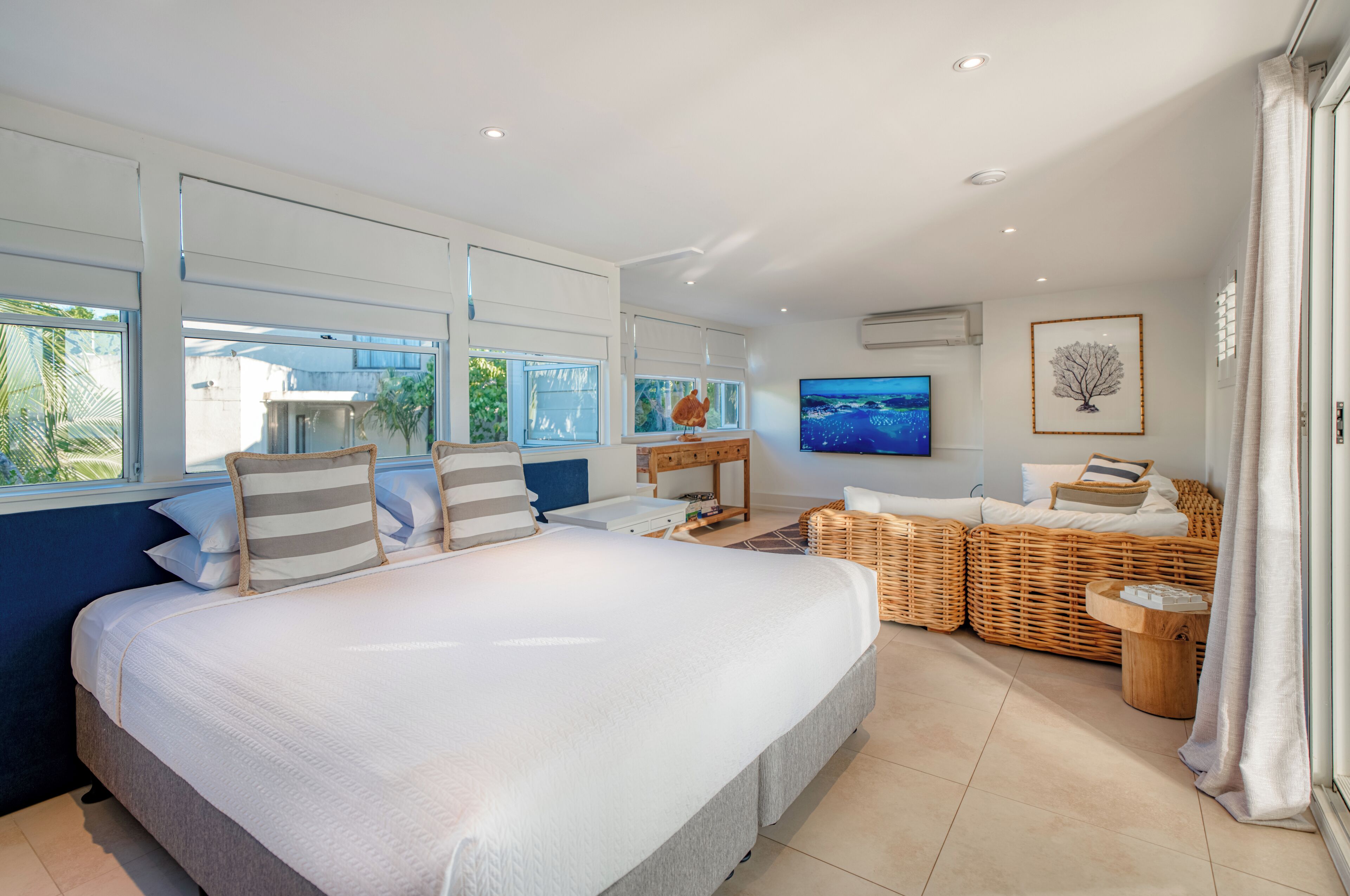 A modern bedroom with a large bed, a TV, wicker furniture, and large windows.