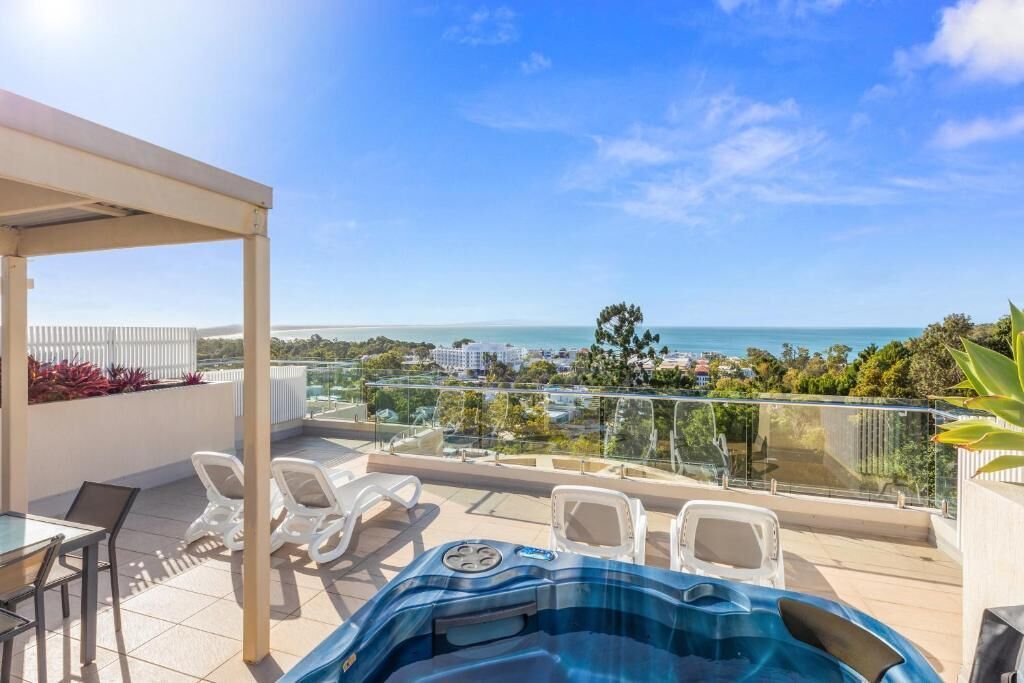 Una terraza en la azotea con jacuzzi, sillones de descanso y vistas al mar y al paisaje urbano.
