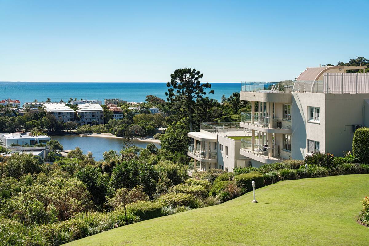 A coastal property with multiple buildings, a large tree, and a view of the sea.