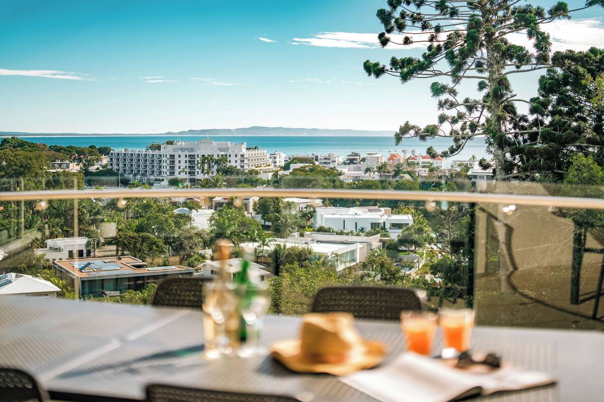 A dining table with a view of a coastal cityscape, including buildings and a body of water.
