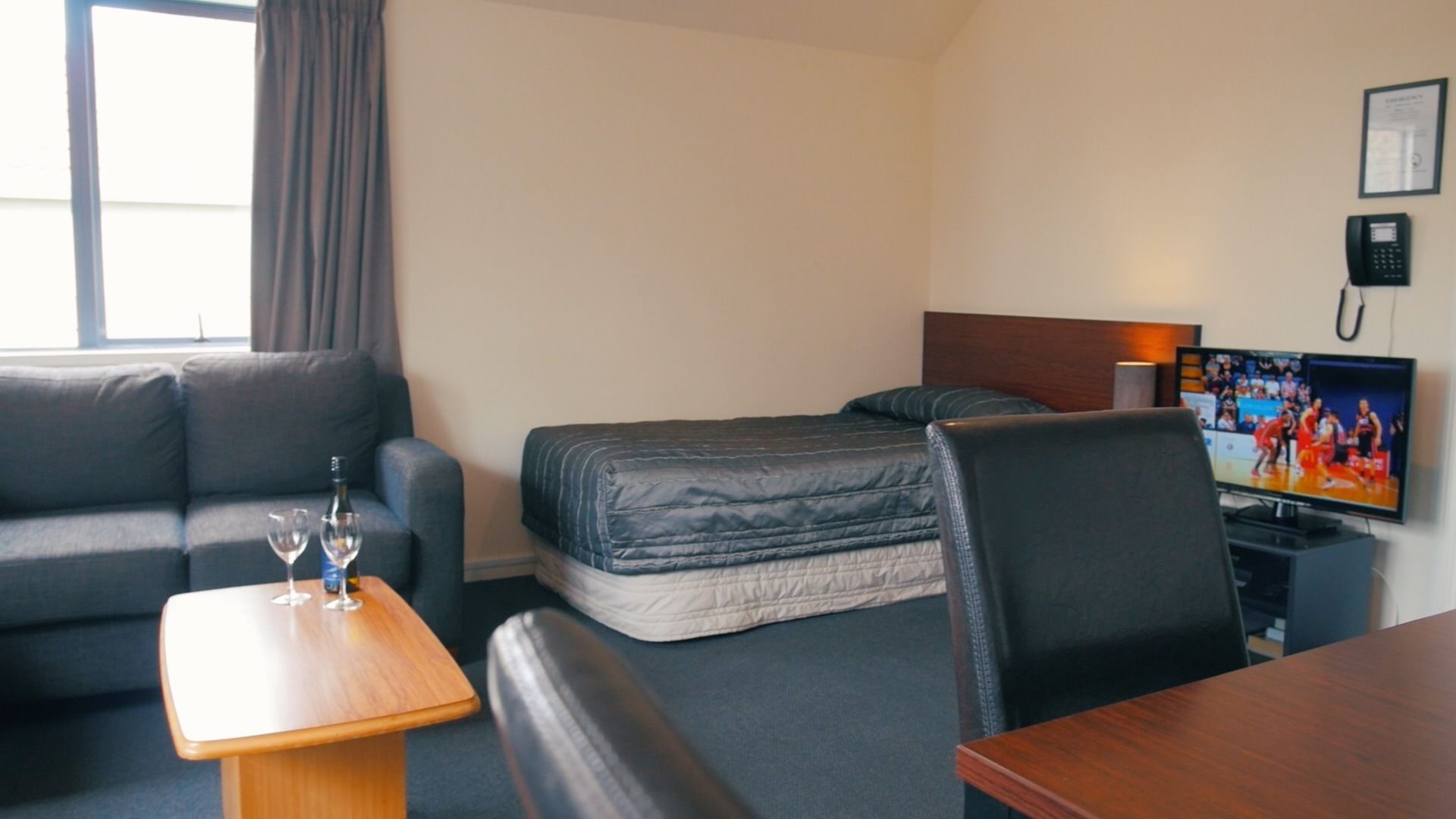 Una habitación de hotel con cama, sofá, televisión, escritorio y ventana con cortinas.