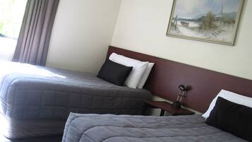 A hotel room with two beds, a painting of a beach scene, and a lamp on a bedside table.