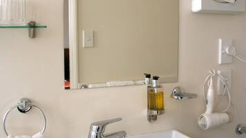 A bathroom with a white sink, a mirror, a towel ring, a glass shelf, and a hairdryer.