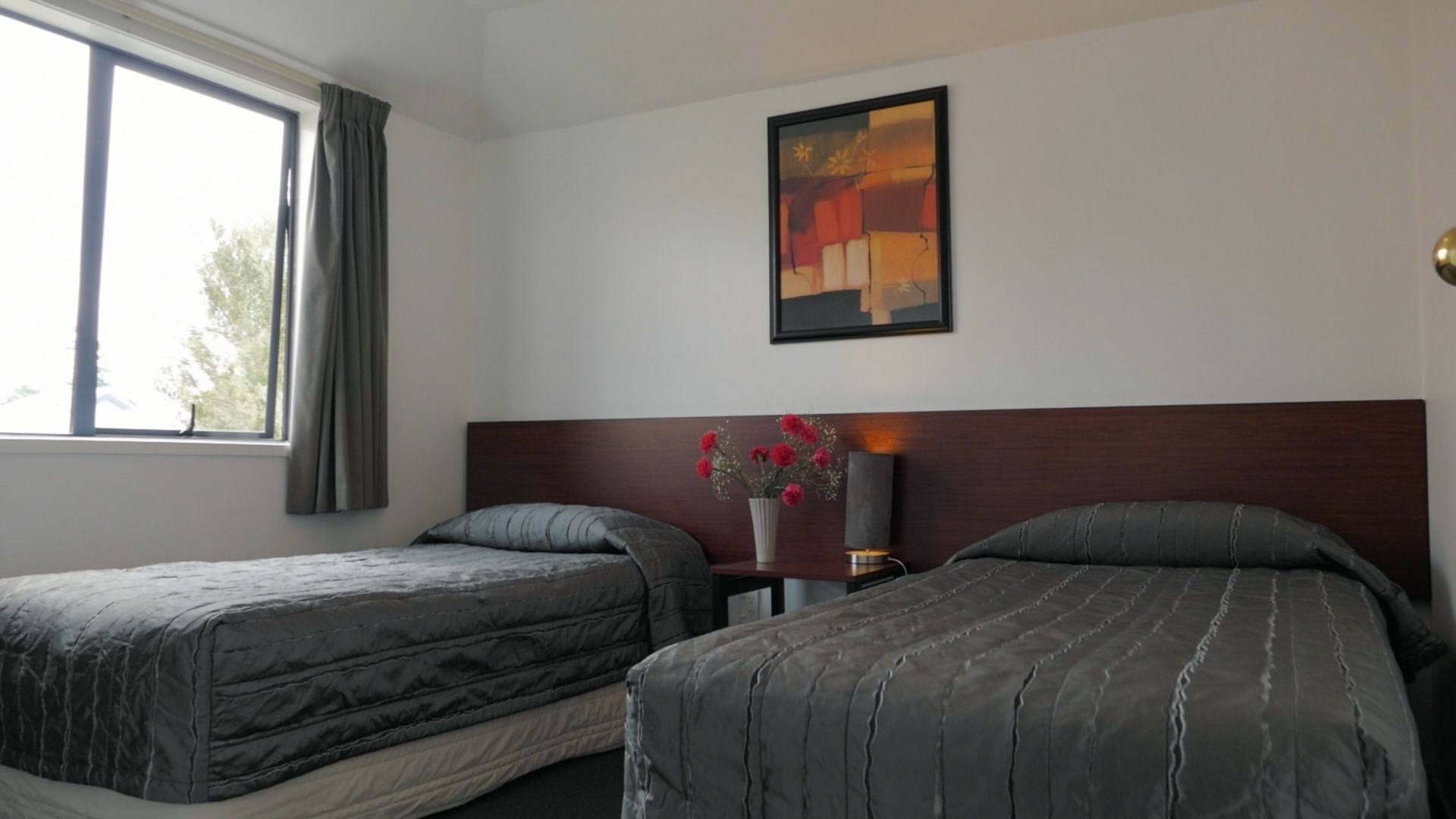 Habitación de hotel con dos camas, una mesita de noche, un jarrón con flores y un cuadro en la pared.