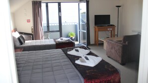 A hotel room with two beds, a sofa, a TV, and a balcony with a plant. - Sherborne Motor Lodge (Christchurch)