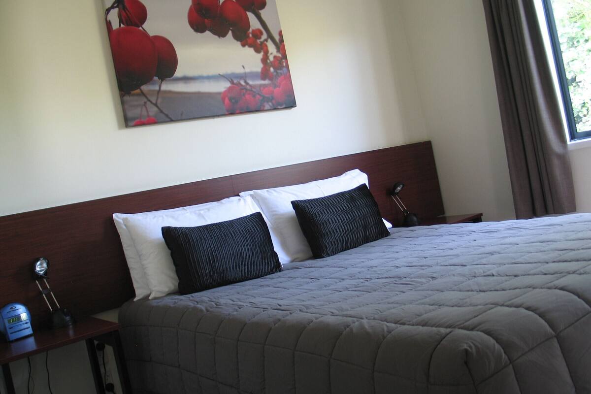 A hotel room with a bed, two pillows, a nightstand with a lamp, and a painting on the wall.