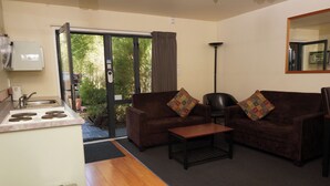 A compact living space with a kitchenette, two sofas with patterned cushions, a coffee table, and a large mirror. - Sherborne Motor Lodge (Christchurch)