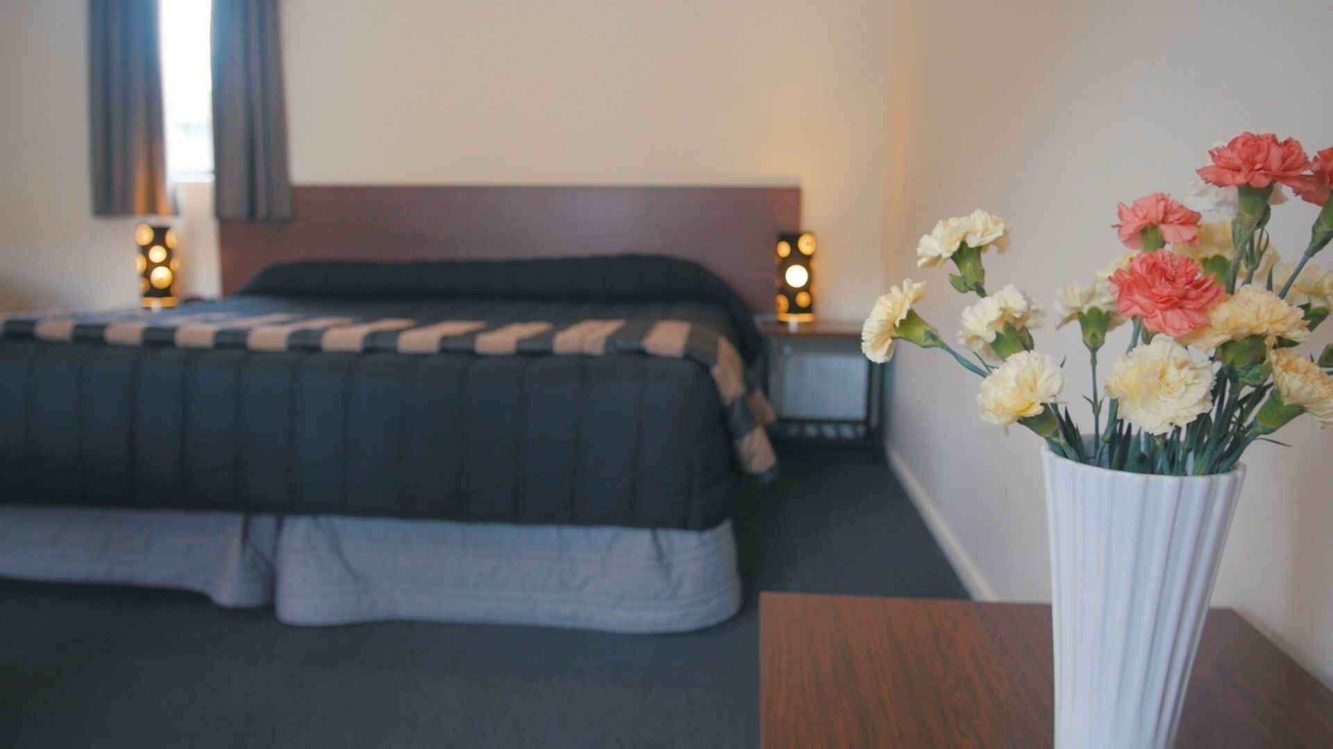 Una habitación de hotel con cama, mesitas de noche y un jarrón de flores.