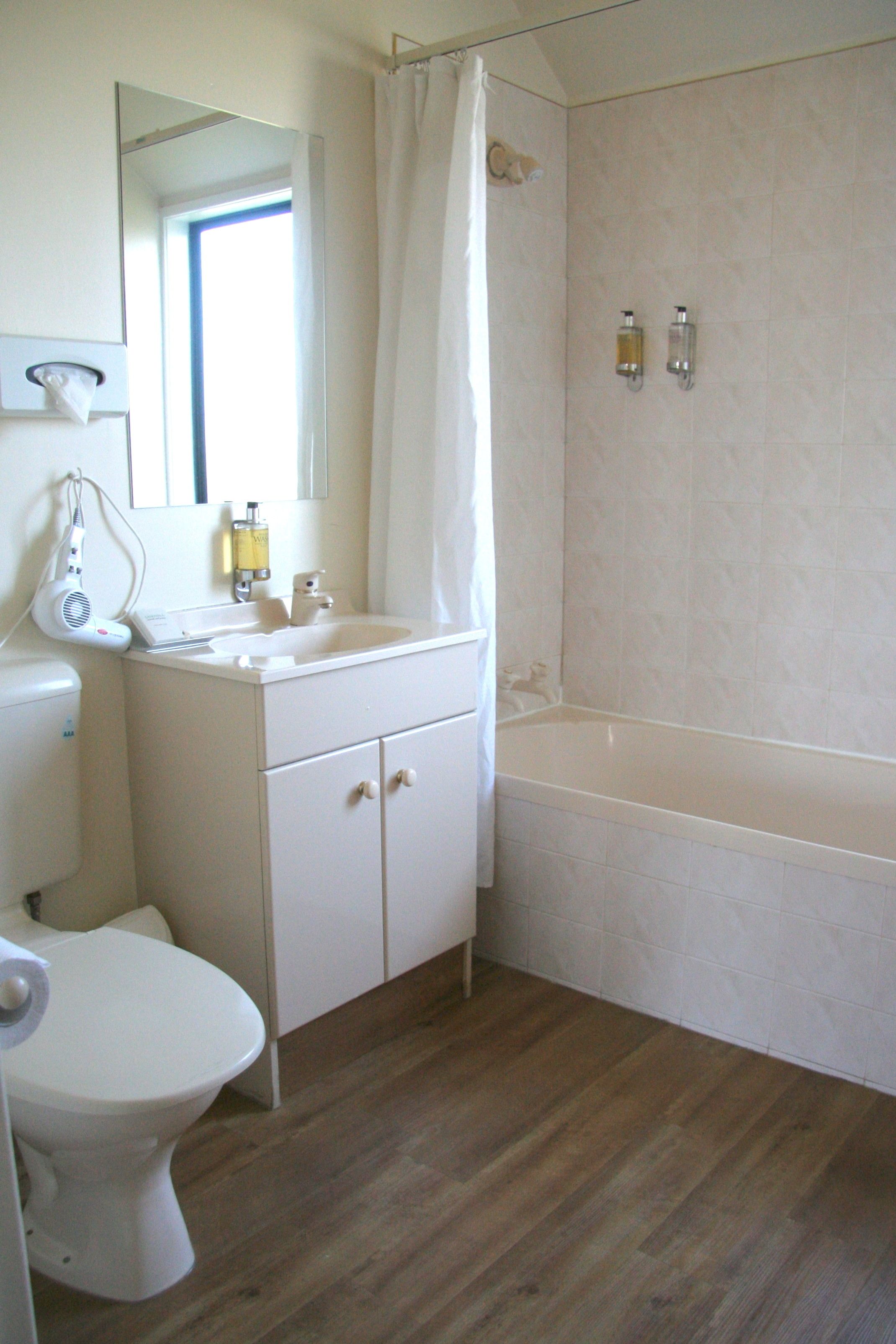 A bathroom with a toilet, sink, mirror, shower curtain, and a bathtub.