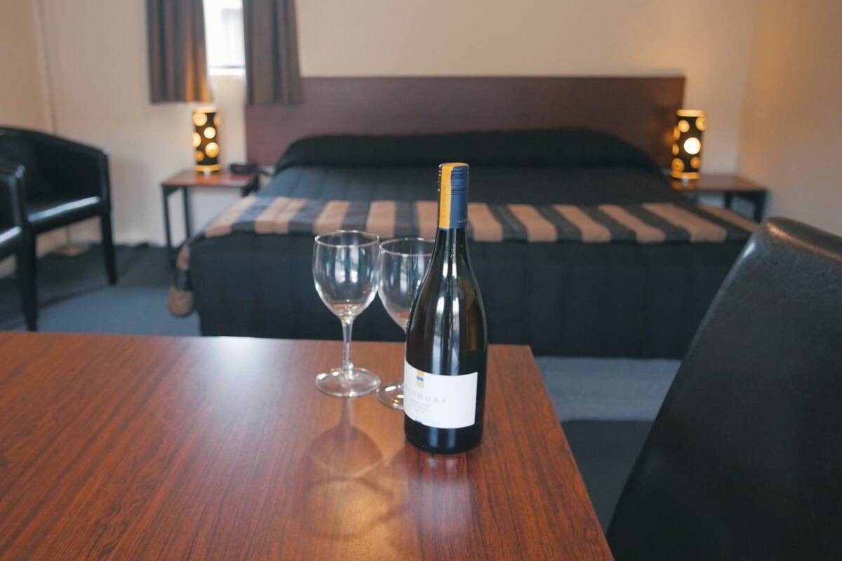 A hotel room with a wooden table, two wine glasses, and a bottle of wine.
