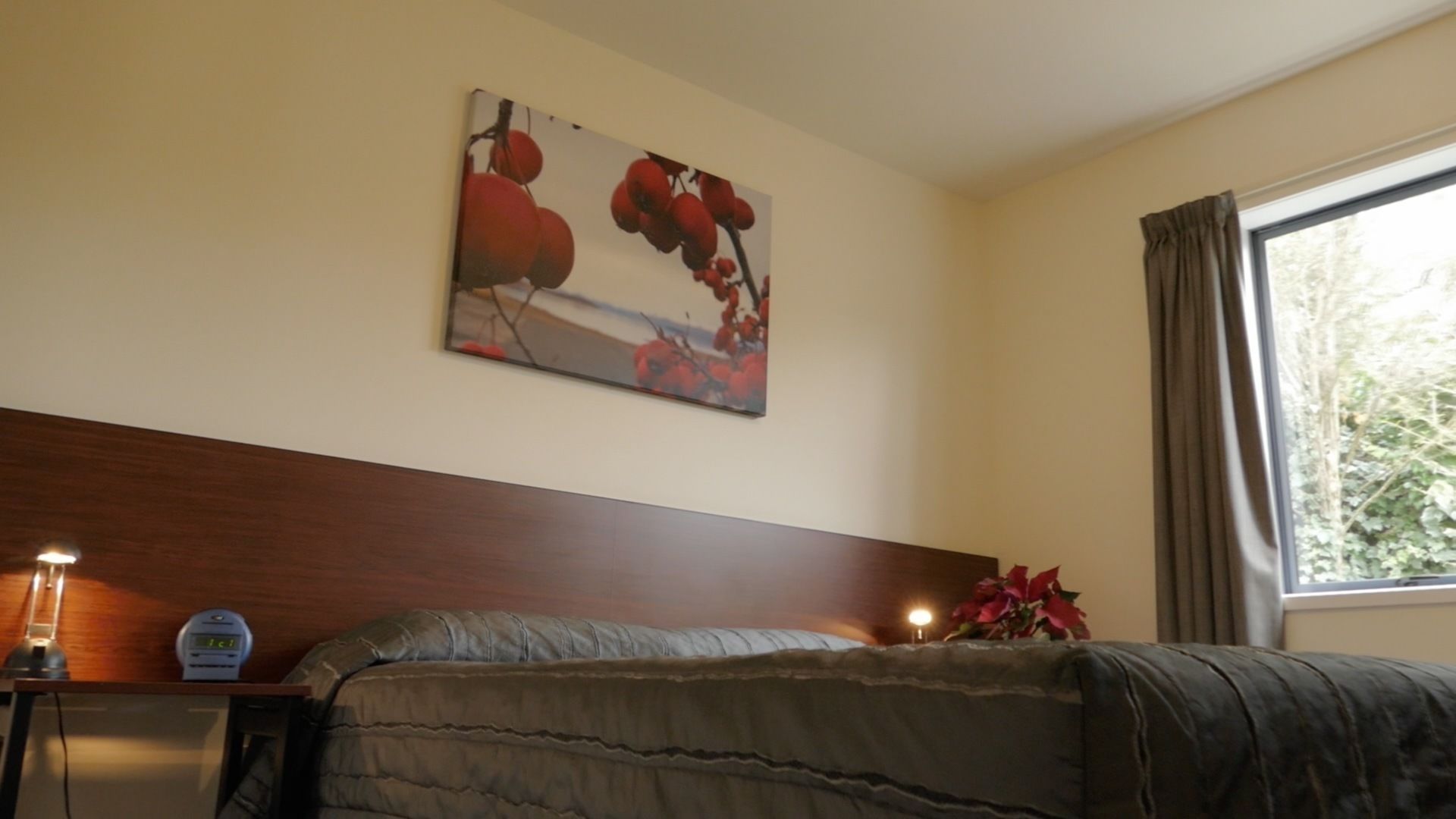 A bedroom with a bed, a nightstand, a wall-mounted painting, a window with curtains, and a bedside lamp.