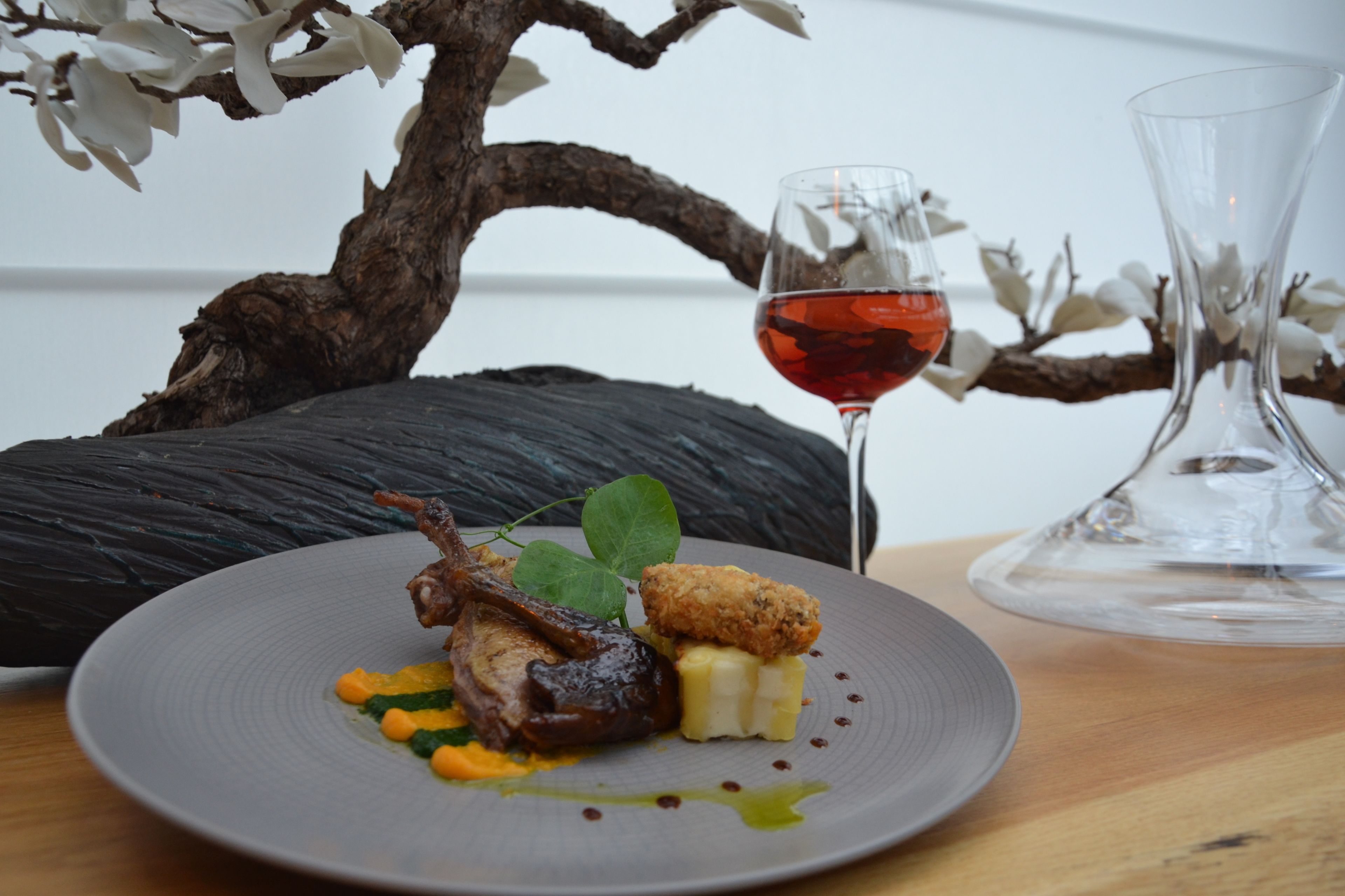 A plate of food with a glass of red wine and a vase on a wooden table.